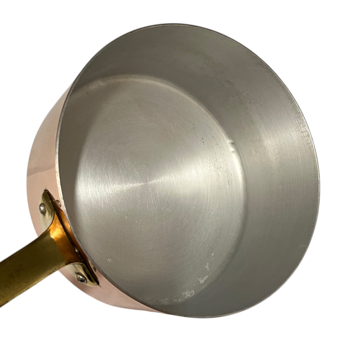Close-up of the interior of a copper saucepan with a brass handle and rivets, set against a plain white background.