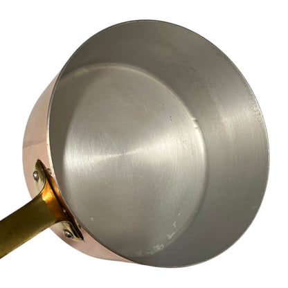 Close-up of the interior of a copper saucepan with a brass handle and rivets, set against a plain white background.