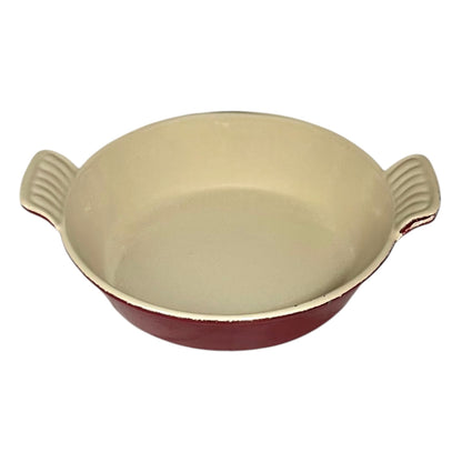 A round enameled cast iron casserole dish with a cream-colored interior and a dark red exterior, featuring two ribbed side handles.