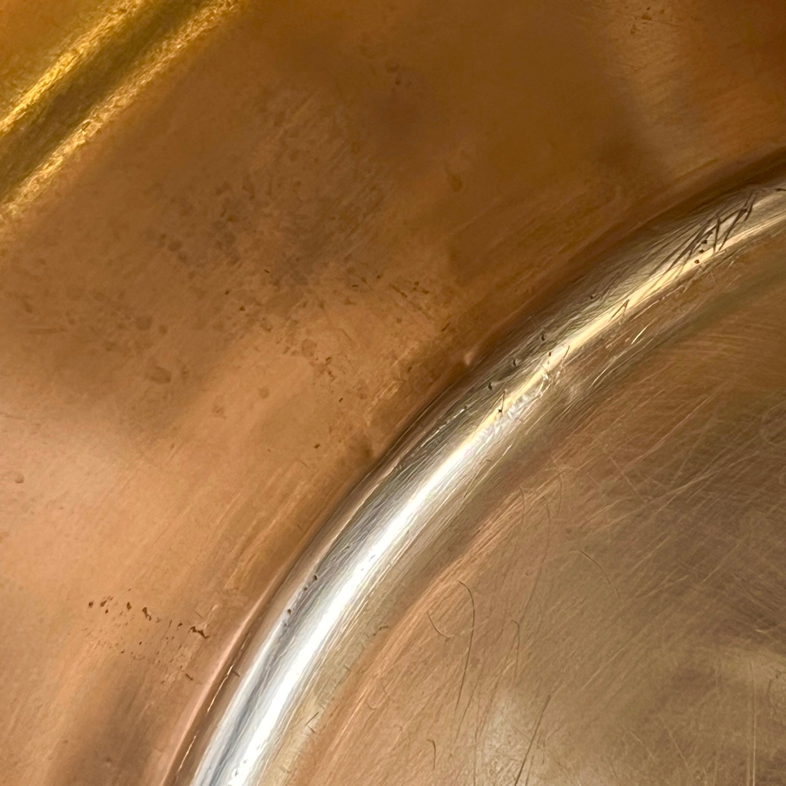 Close-up of the interior of a copper sink or basin, showing a brushed metallic surface with a polished curved rim.