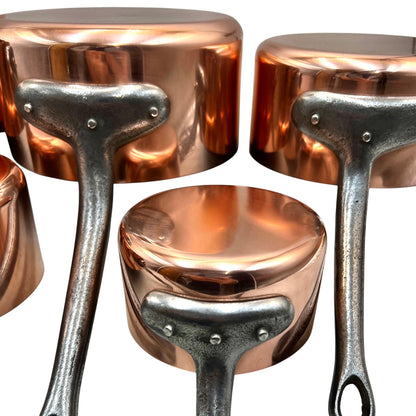 A set of copper saucepans with dark forged steel handles, shown in close-up against a white background.