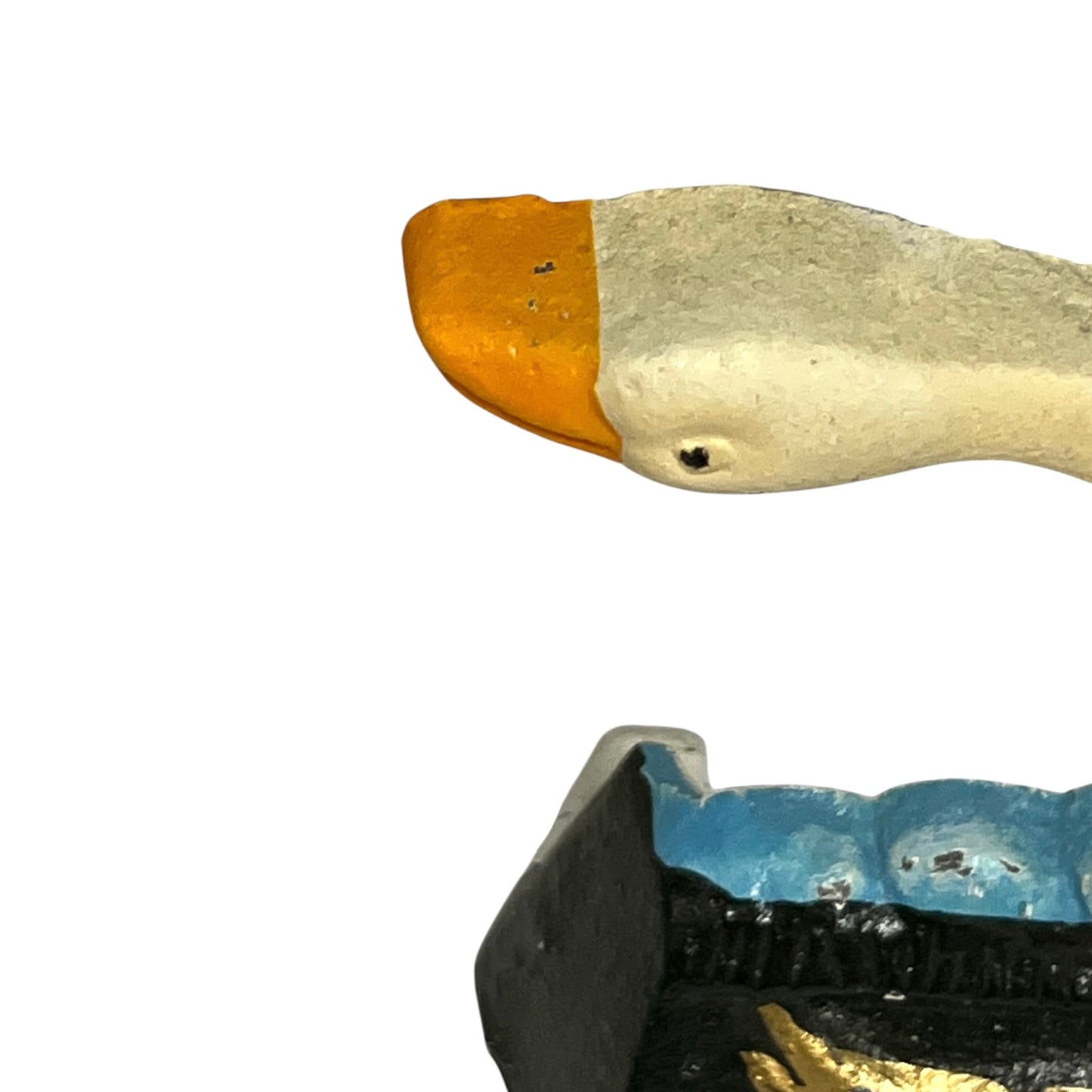A close-up of a hand-painted duck figurine on a plain white background, showing its orange beak, cream-colored body, and a blue and black painted landscape below.