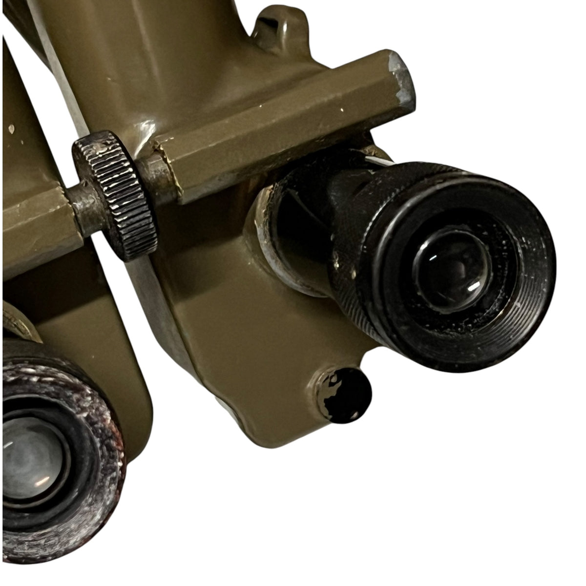 Close-up of an olive green and black optical device, showing part of the body with adjustment knobs and lenses, isolated on a white background.