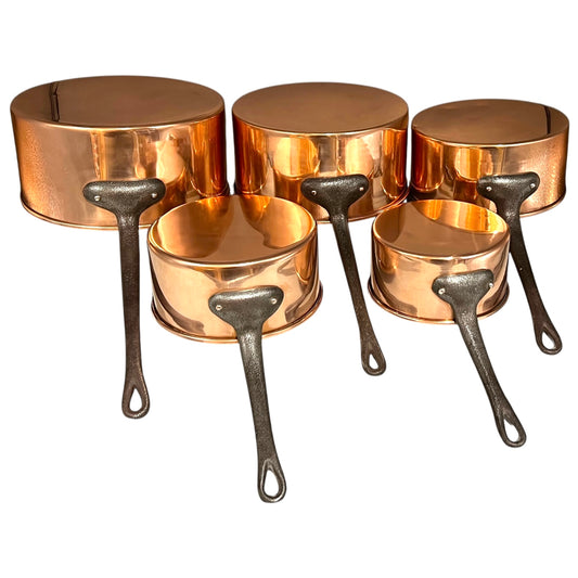 Set of five French copper saucepans with iron handles on a white background