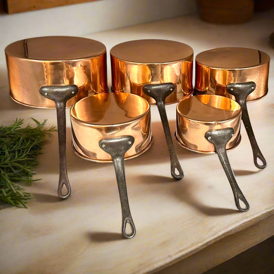 Set of copper saucepans with cast iron handles on a marble surface.