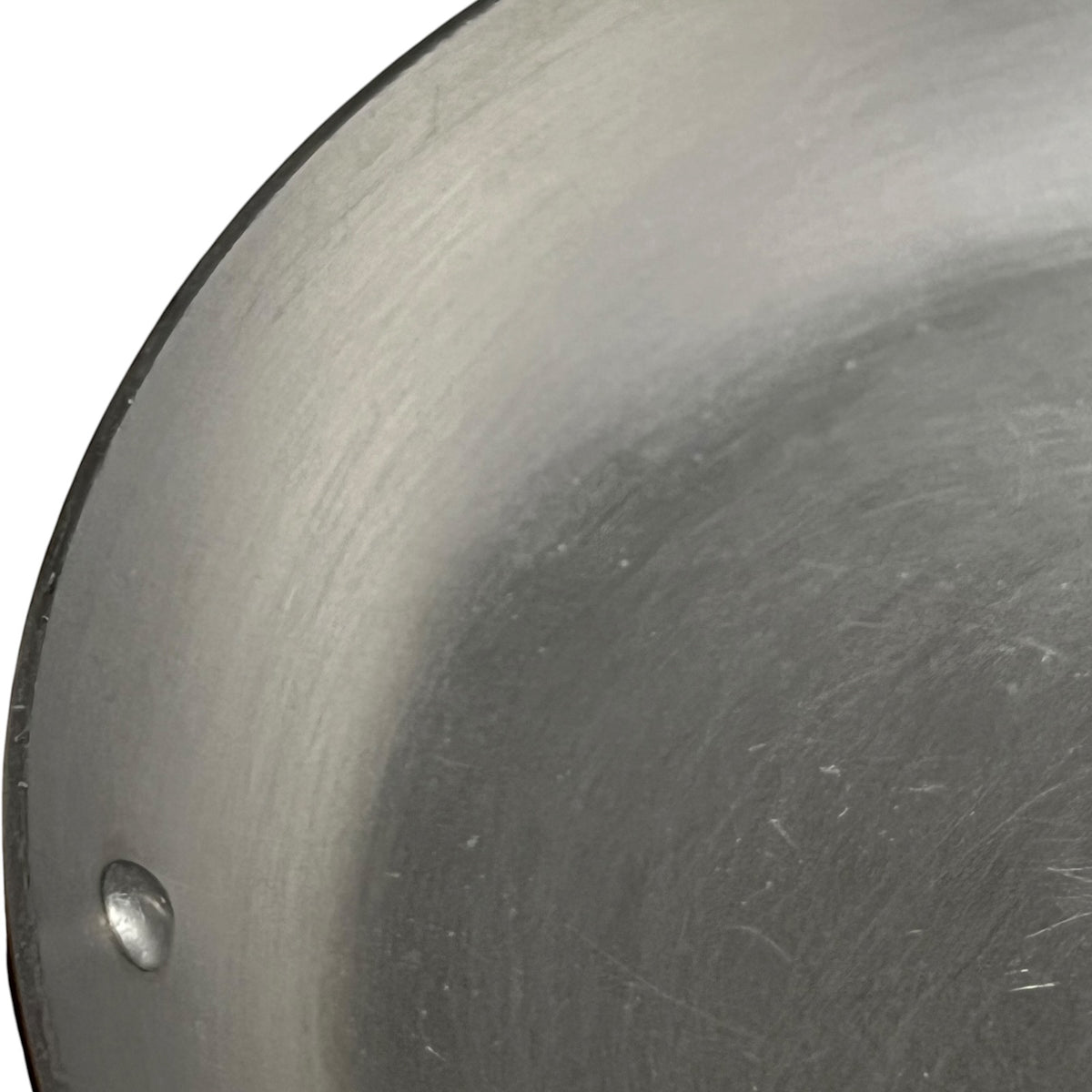 Close-up of a aluminium cookware surface showing the interior wall and a small rivet, photographed against a white background.
