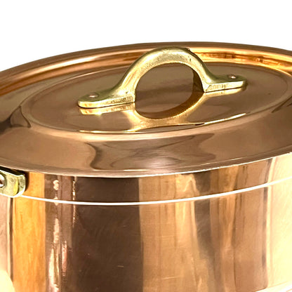 Close-up of a copper lid with a handle on a copper casserole pot