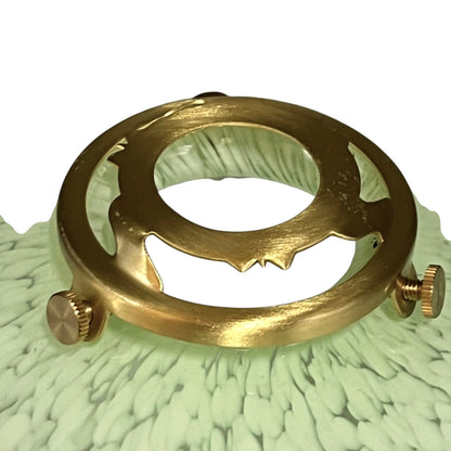 A brass circular ring-shaped accessory with two small knurled adjustment knobs, photographed on a pale green textured surface against a white background.