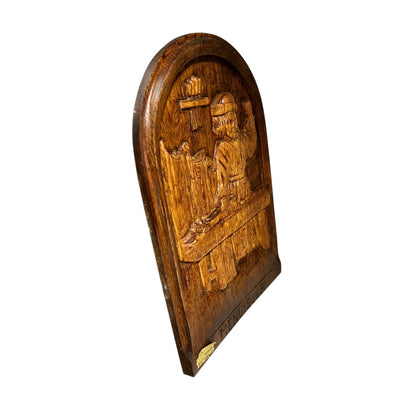 Wooden plaque with a carved design of a person playing a musical instrument on a white background