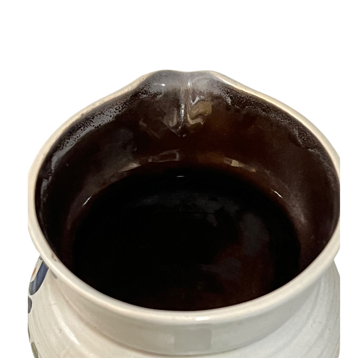Close-up of the interior of a ceramic pitcher or small vase, showing a glossy dark brown glazed surface inside a white ceramic body on a plain white background.