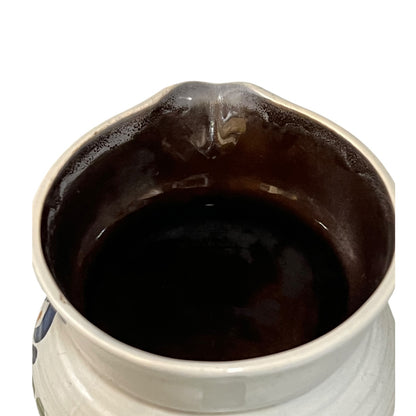Close-up of the interior of a ceramic pitcher or small vase, showing a glossy dark brown glazed surface inside a white ceramic body on a plain white background.