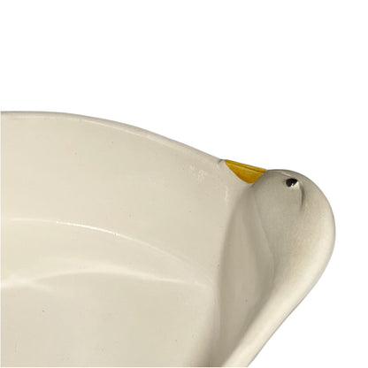 Close-up of a white ceramic duck-shaped bowl or dish with a small yellow beak detail and a black eye, shown against a plain white background.
