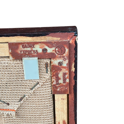 Close up of framed tapestry needlepoint with a coastal scene and wooden frame on a white background