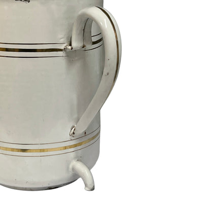A close-up of a white ceramic pitcher or mug with a curved handle, a small spout, and thin gold decorative stripes on a white background.