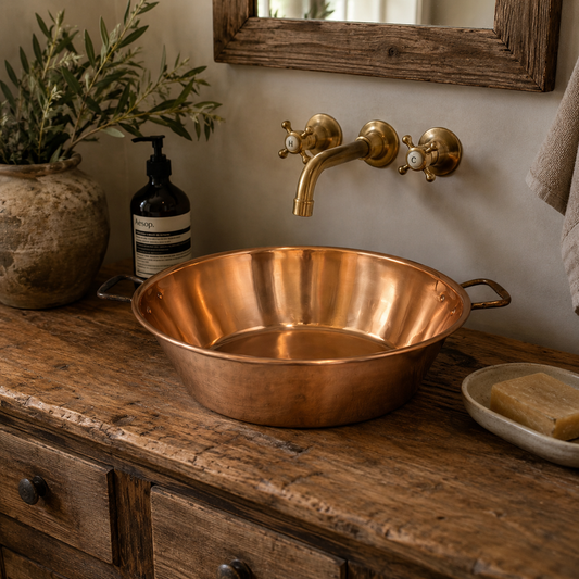 French upcycled copper basin sink with side handles and a chrome-topped drain, perfect for adding charm to a rustic bathroom, camper van, or cloakroom, displayed on a rustic wooden vanity in a traditional bathroom