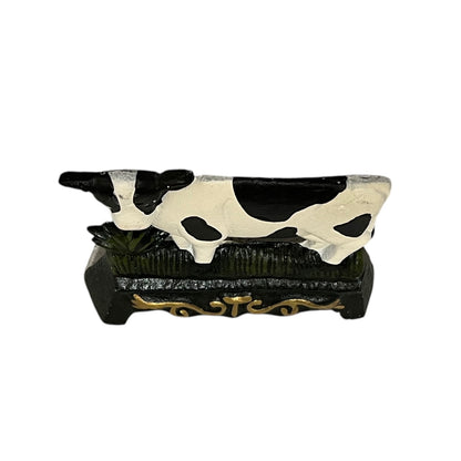Close up of small cow shaped cast iron doorstop on a white background