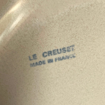 Close-up of a beige ceramic surface with blue printed text reading 'LE CREUSET MADE IN FRANCE'.