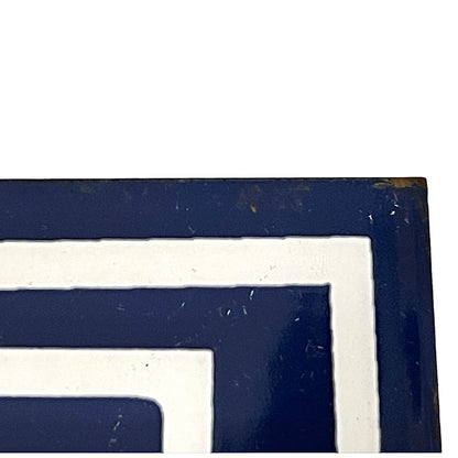 A close-up of a geometric patterned surface with alternating thick navy blue and off-white concentric border shapes, showing some wear and scuffs on the glossy finish.