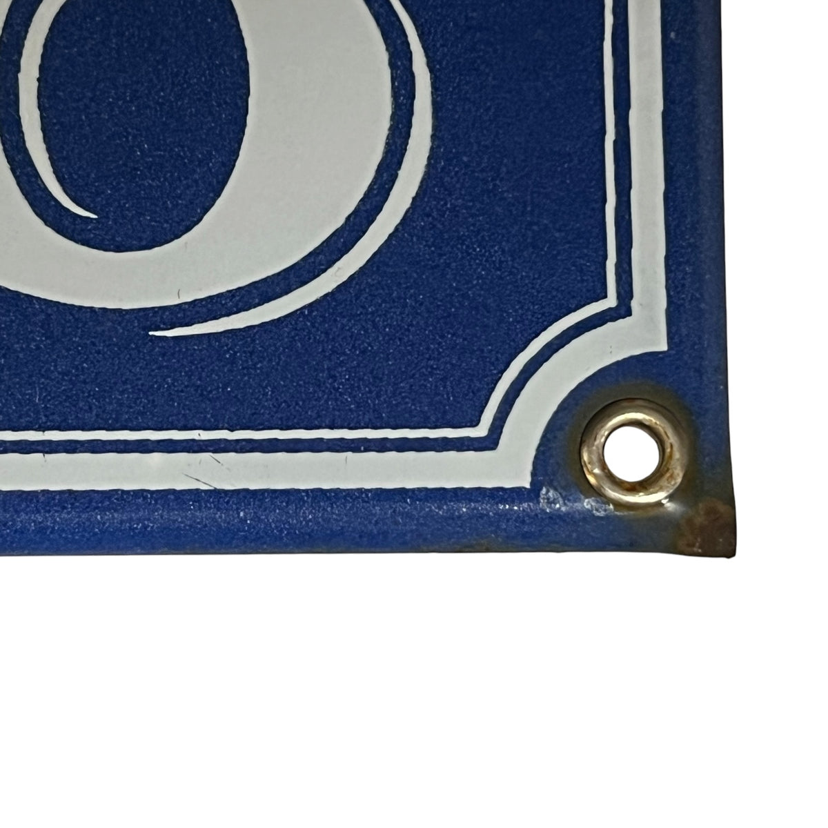 Close-up of a blue and white sign corner with a metal grommet, showing part of a white circular emblem on a blue background.