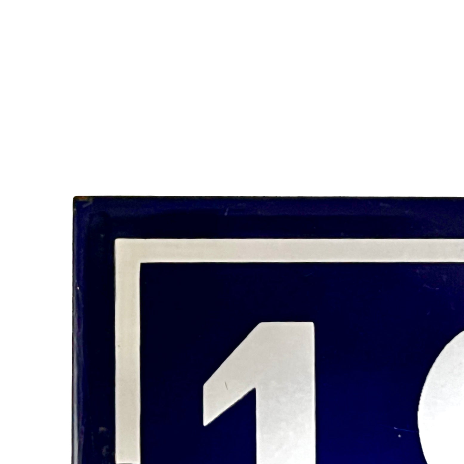 Close-up of a dark blue square sign or plaque with a white border and a large white number 1 visible, against a white background.