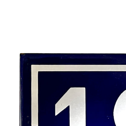 Close-up of a dark blue square sign or plaque with a white border and a large white number 1 visible, against a white background.