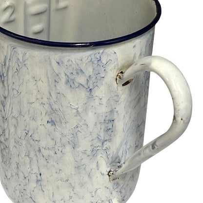 A close-up of a vintage enamel storage pot with a white marbled blue pattern, a dark blue rim, and a white handle.