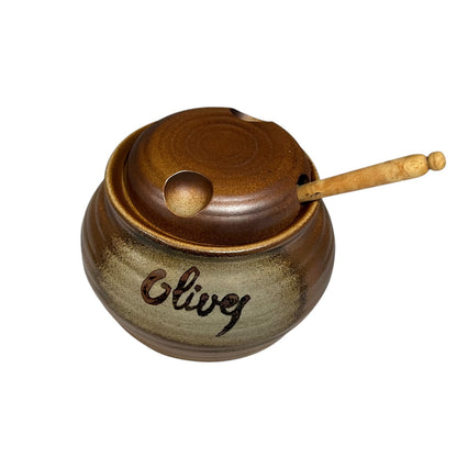A brown stoneware ceramic olive pot with a wooden spoon, set against a white background, perfect for adding charm to a country cottage.