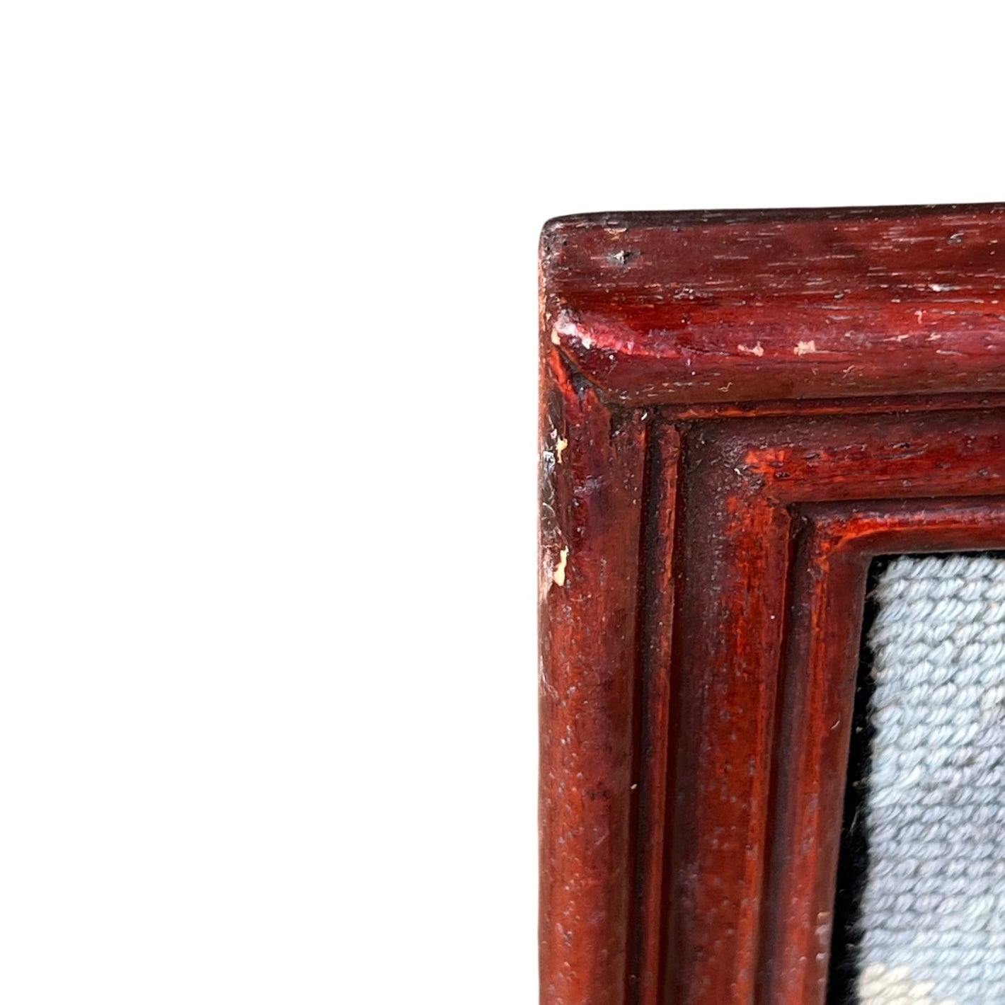 Close up of framed tapestry needlepoint with a coastal scene and wooden frame on a white background