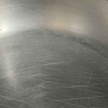 Close-up of a scratched metallic surface, likely a stainless steel pan or pot interior, showing visible scuffs and wear marks.