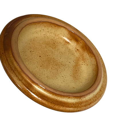 An oval ceramic lid with a glossy, speckled glaze in shades of brown and beige, shown on a plain white background.