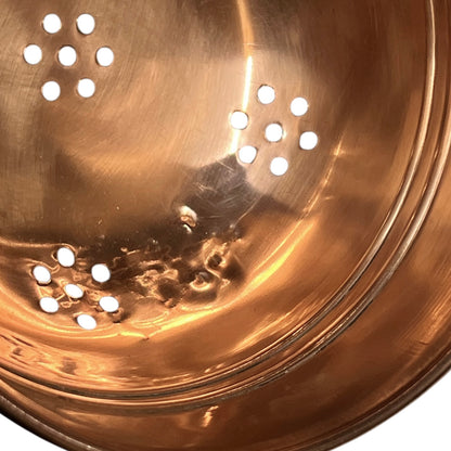 Close up of a small copper French sieve with a brass handle on a white background