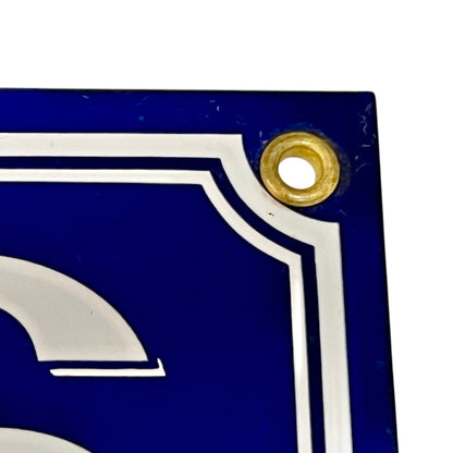 Close-up of a blue sign with white letter 'S' and gold accent on a white background