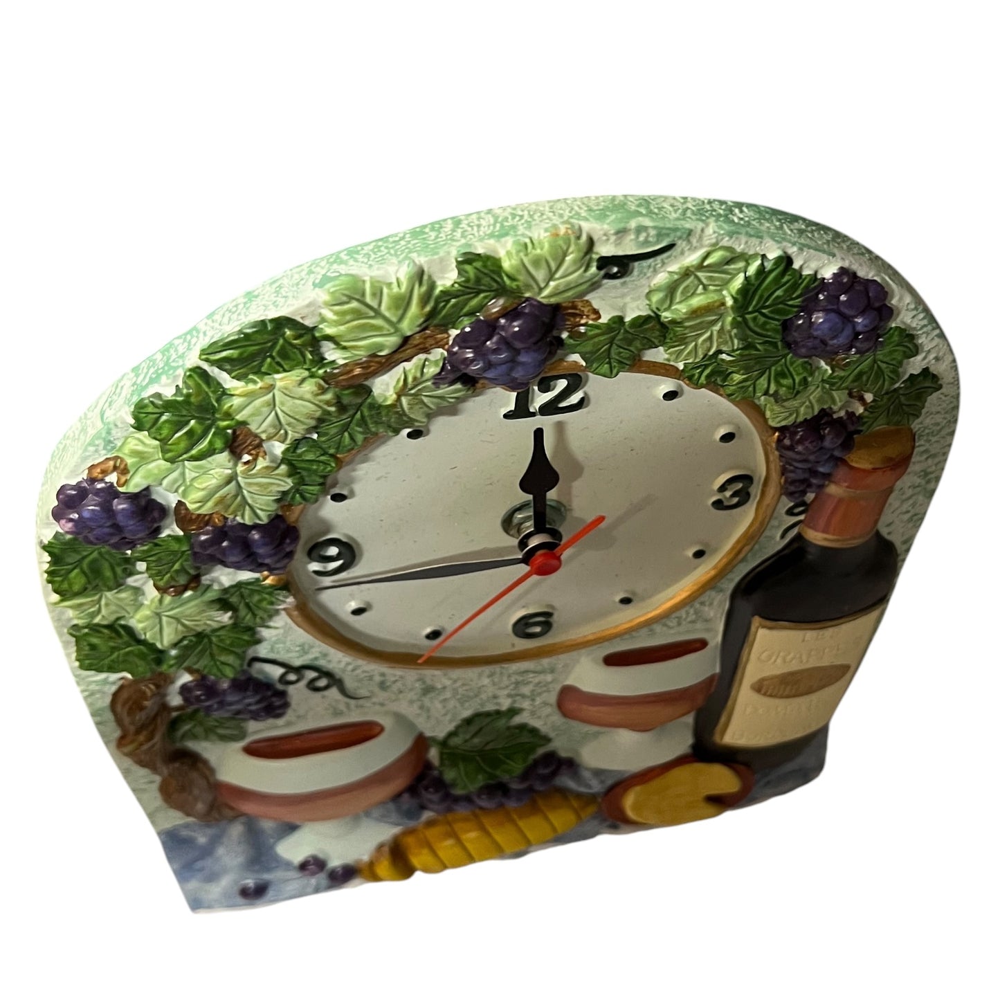 A decorative tabletop clock with a wine-themed design, featuring green leaves and purple grapes around a white clock face, plus a wine bottle and glasses on the front.