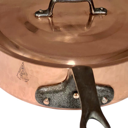 Close-up of a copper pot with a lid and handle, featuring a brand logo.