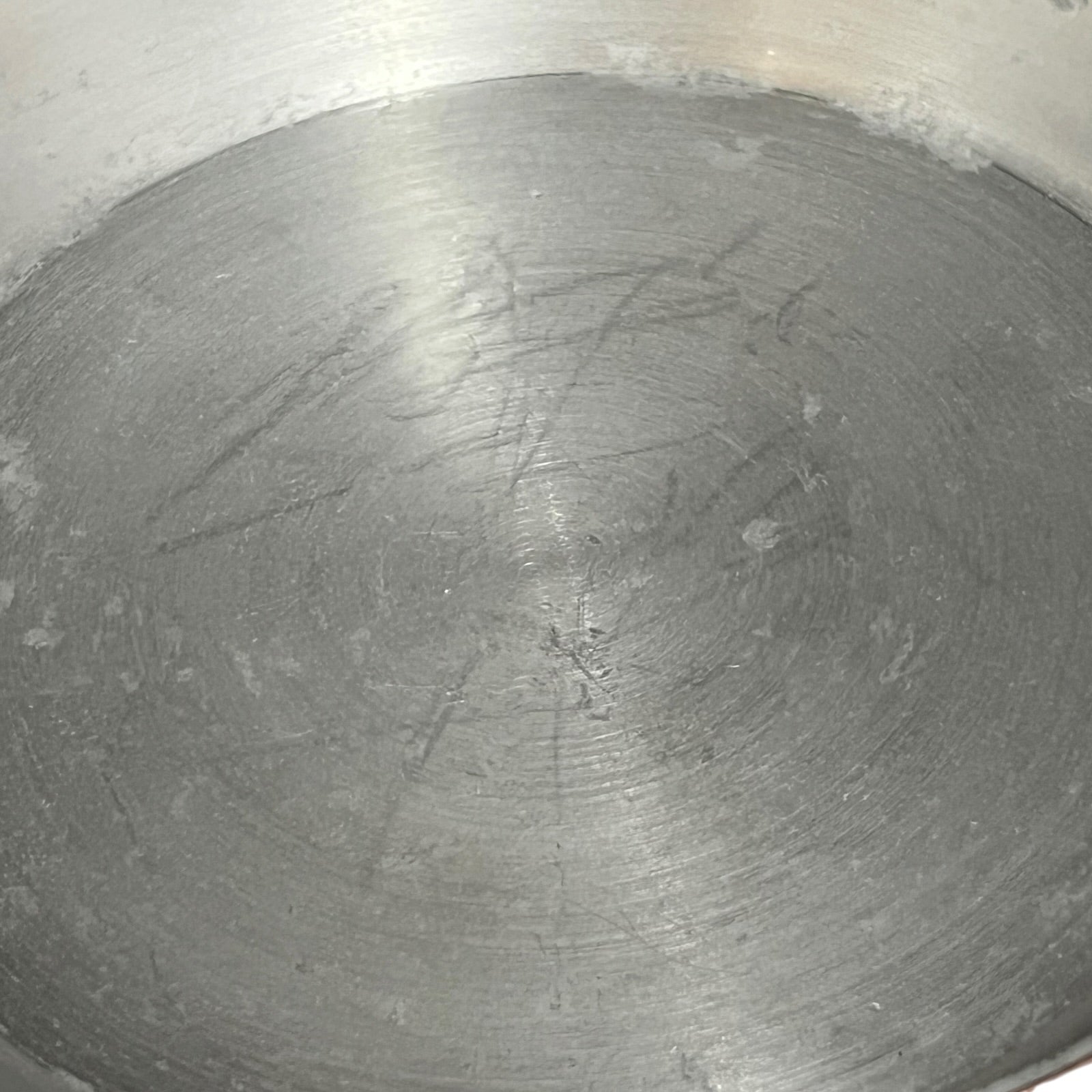 The inside of a used stainless steel pot or pan, showing a circular brushed metal surface with visible scratches and wear.
