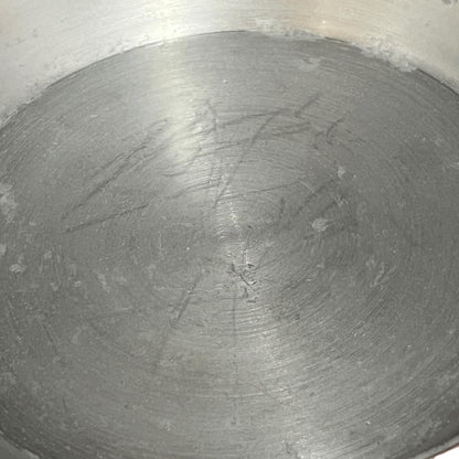 The inside of a used stainless steel pot or pan, showing a circular brushed metal surface with visible scratches and wear.