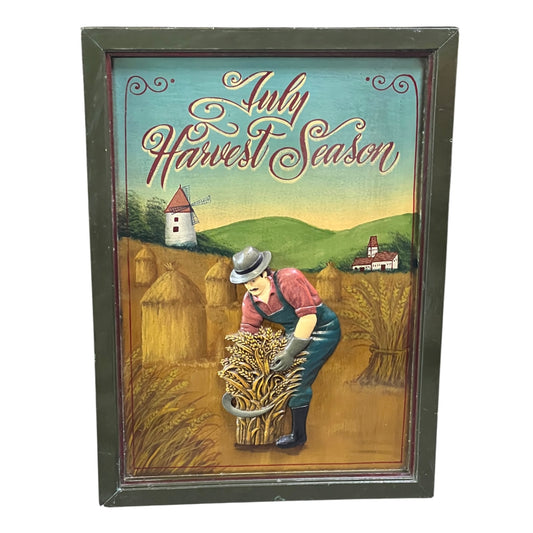Decorative sign with a farmer and 'July Harvest Season' text, framed.