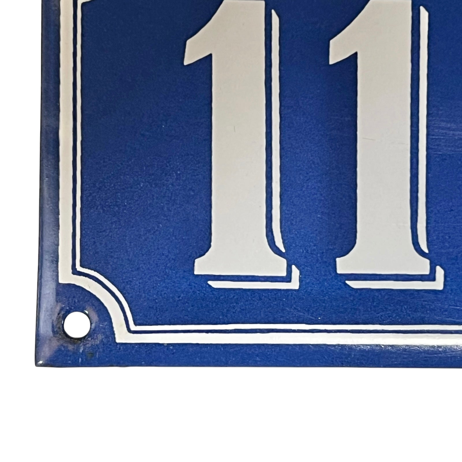 Close up of a blue French metal house number plate with white numbers '111' on a white background