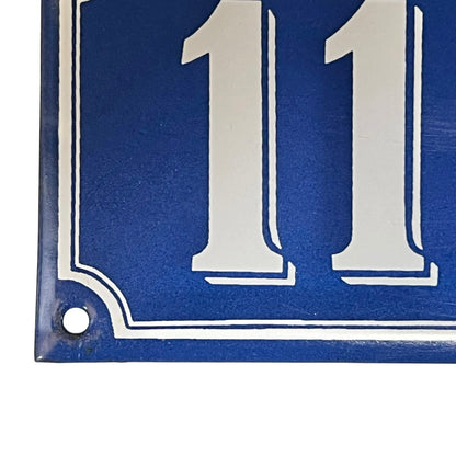 Close up of a blue French metal house number plate with white numbers '111' on a white background