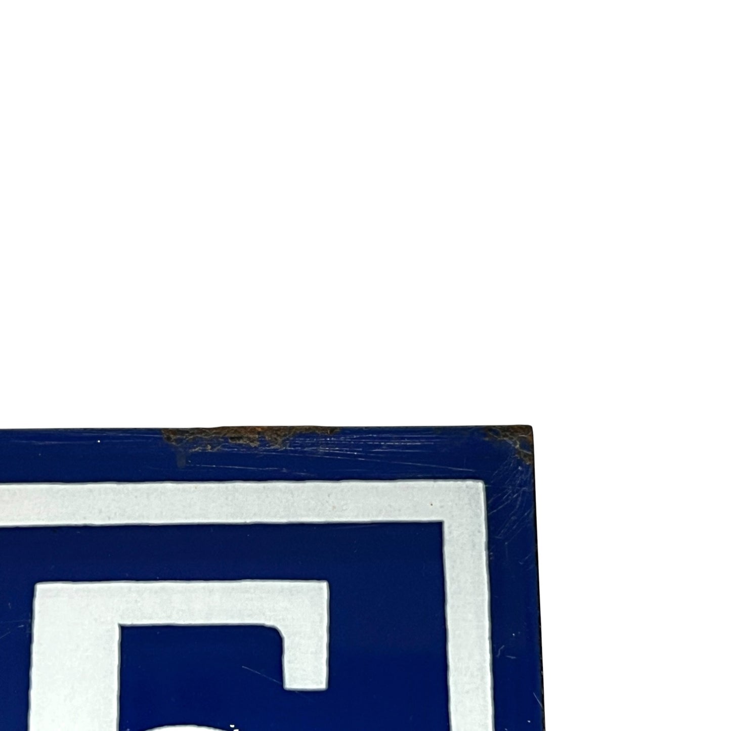 A close-up of a blue and white square sign or plaque corner with a distressed finish, shown against a white background.