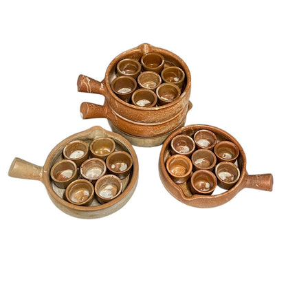 Three rustic brown ceramic serving pots with handles, each containing multiple small matching cups, arranged on a plain white background.