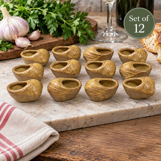 Set of 12 small ceramic cup-shaped bowls with a textured grain pattern, arranged on a marble serving board with garlic, parsley, bread, and a wine glass in the background.