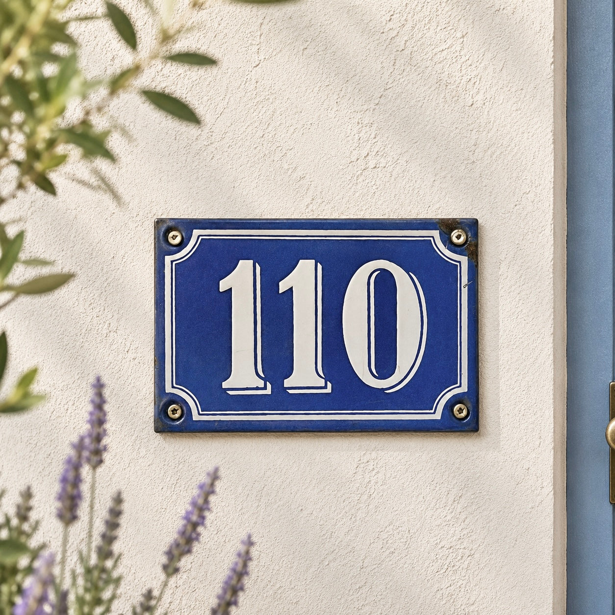 French blue and white enamel door number in vintage enamel shown mounted on a whitewashed wall with a blue door and lavender in the background 