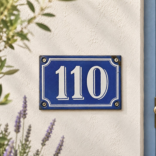 French blue and white enamel door number in vintage enamel shown mounted on a whitewashed wall with a blue door and lavender in the background 
