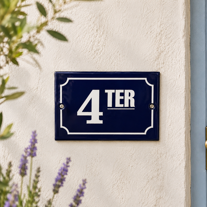 Navy blue house number sign with '4 TER' on a white wall, surrounded by greenery.