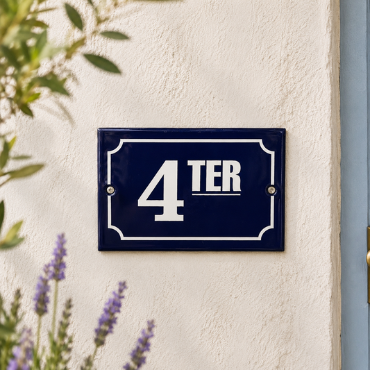 Navy blue house number sign with '4 TER' on a white wall, surrounded by greenery.