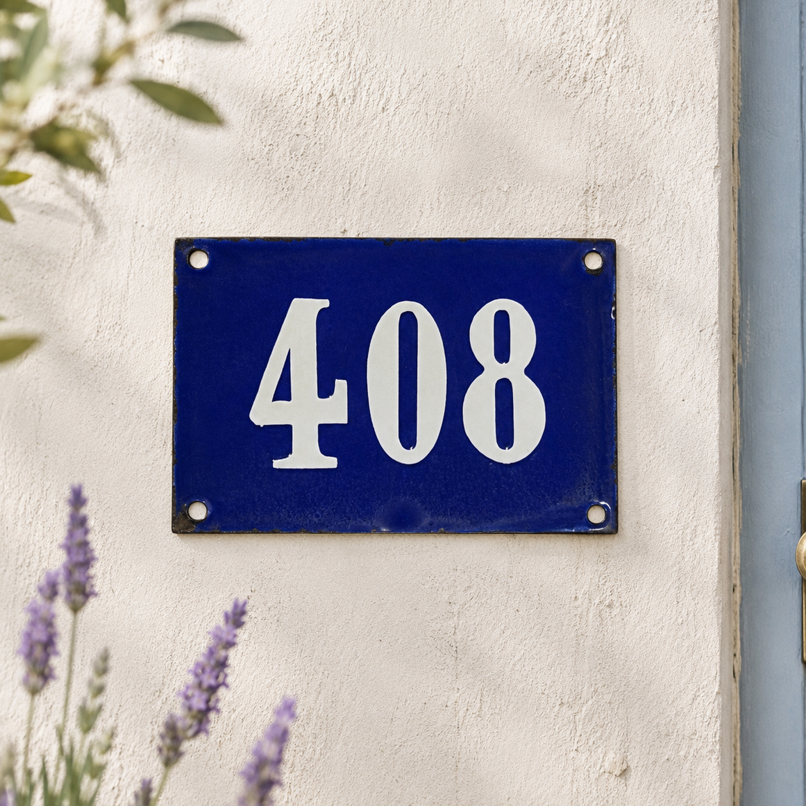 Blue enamel French-style house number plaque displaying the number 408 in white, mounted on a cream rendered exterior wall with visible fixing screws. Soft-focus lavender flowers and leafy branches frame the sign in natural daylight.