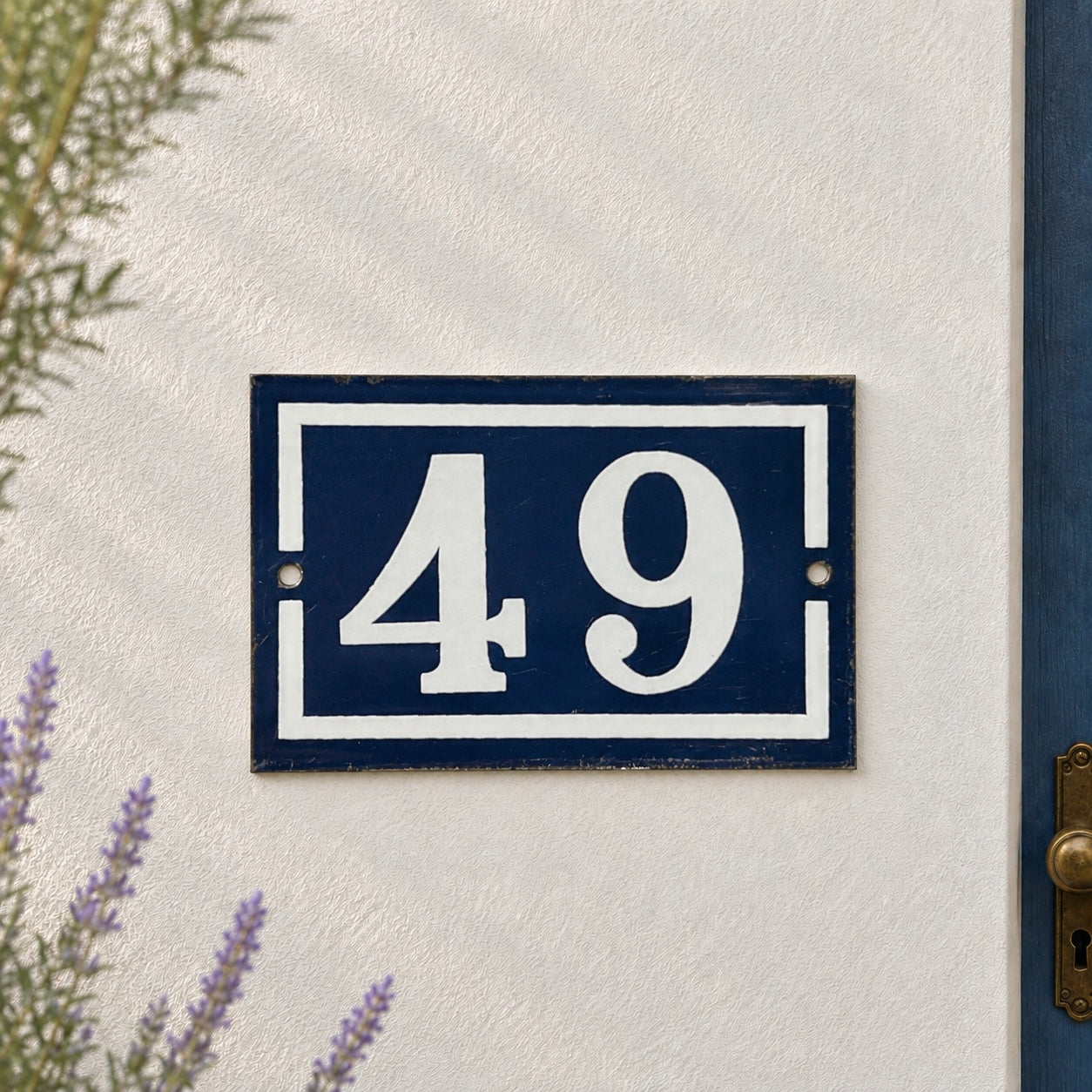 French enamel vintage blue and white door house number 49 displayed on a whitewashed wall with lavender in the background 