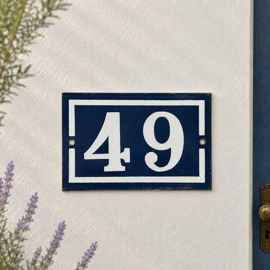 French enamel vintage blue and white door house number 49 displayed on a whitewashed wall with lavender in the background 
