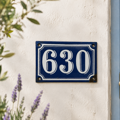 Blue house number plate with '630' on a white wall with lavender plants.